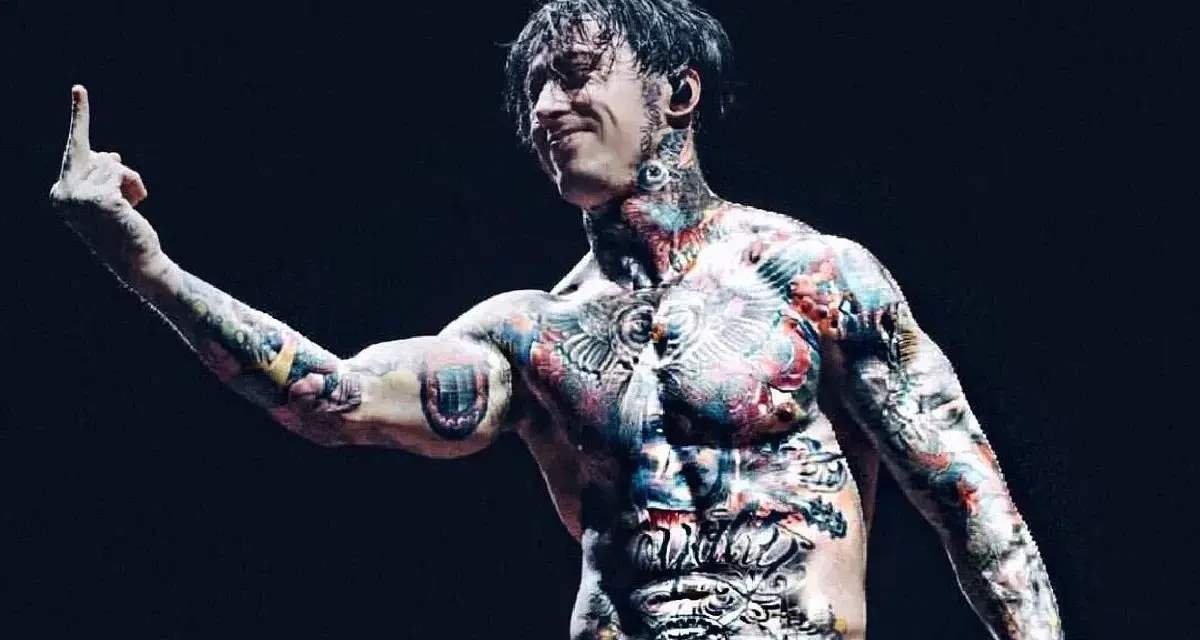 Le chanteur de Falling In Reverse, Ronnie Radke, torse nu et couvert de tatouages colorés, lève le majeur sur scène.