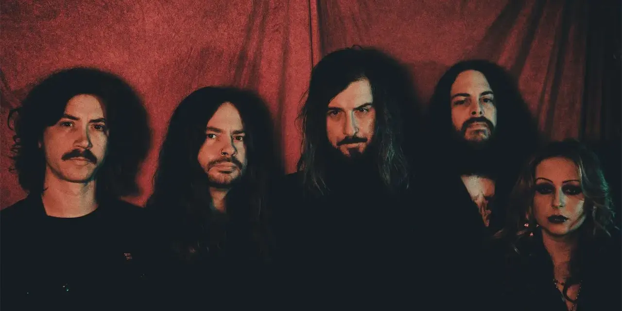 Cinq membres du groupe Uncle Acid and the Deadbeats posent devant un rideau rouge.