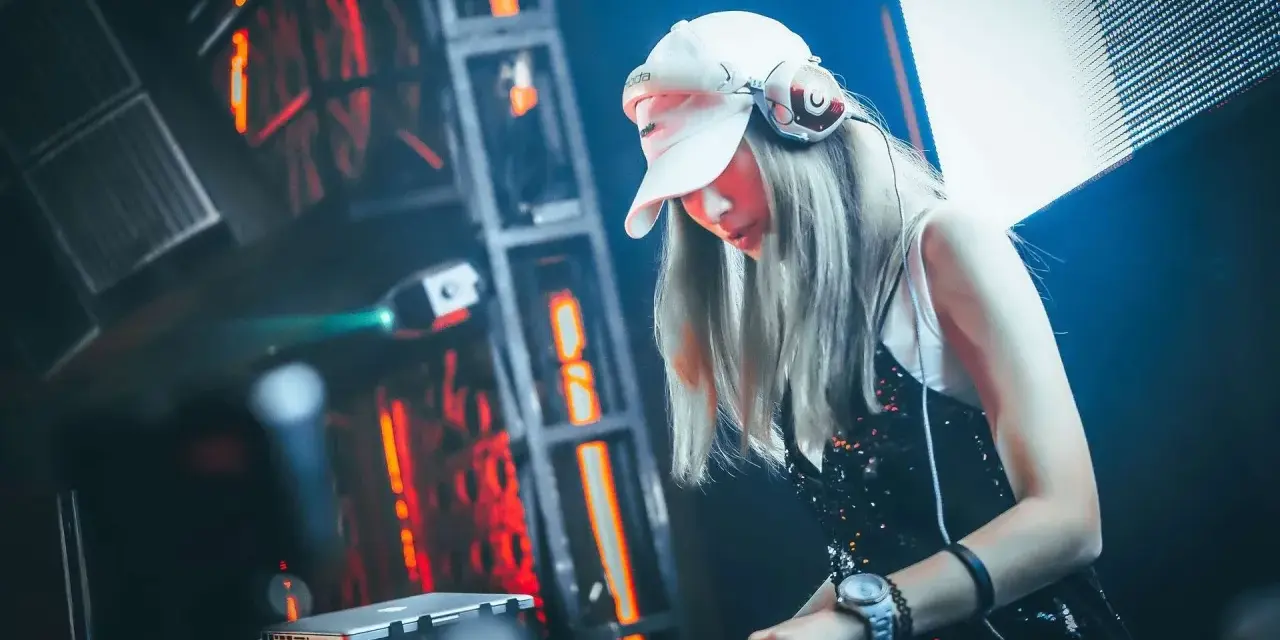 Une dj femme, casquette blanche et casque sur les oreilles, mixe dans une ambiance lumineuse et électrique.