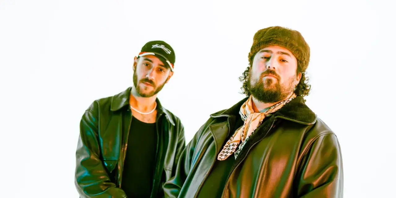 Deux DJ les plus connus, l'un porte une casquette et l'autre un bonnet en fourrure, posent devant un fond blanc.