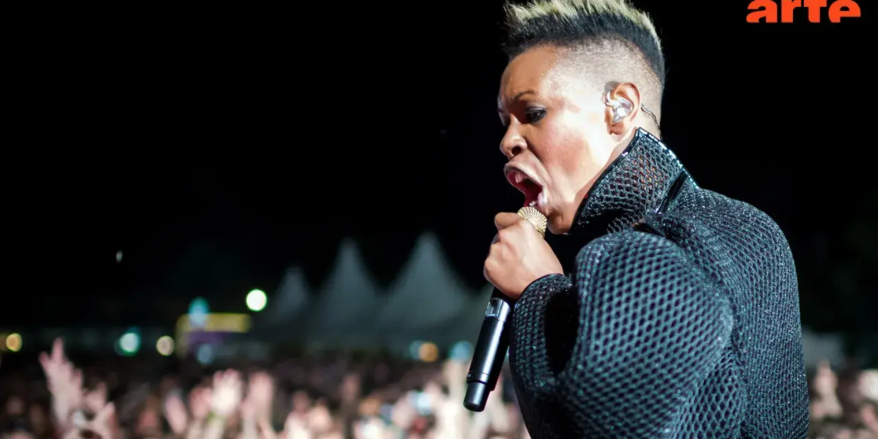 Skunk Anansie en pleine performance, micro d'or à la main, devant une foule en délire. La chanteuse captive avec son énergie.