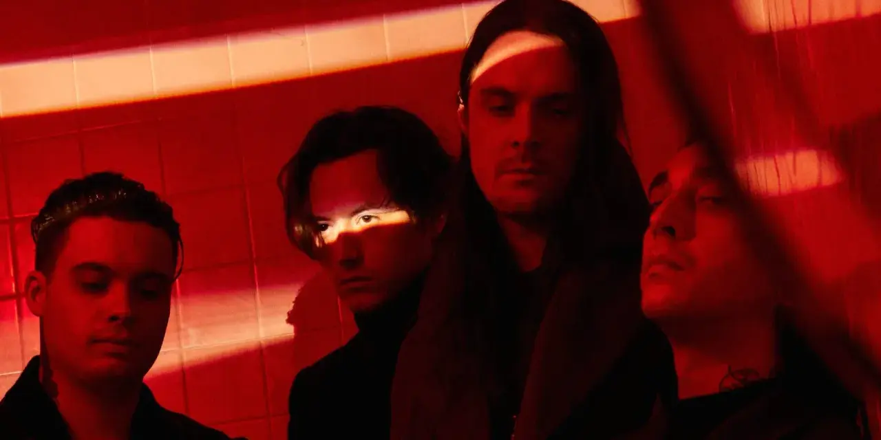 Les membres de Bad Omens posent dans une ambiance rouge intense, éclairés par des ombres dramatiques.
