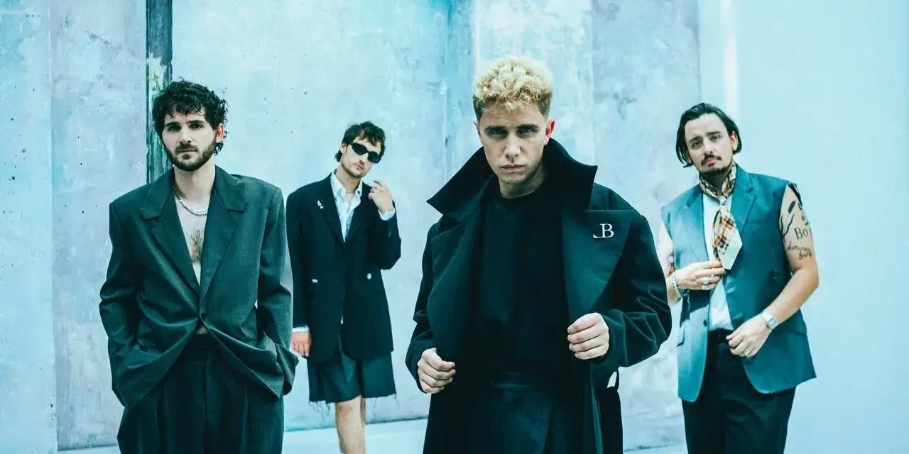 Le groupe Last Train pose devant un mur bleu clair, quatre hommes aux styles audacieux.