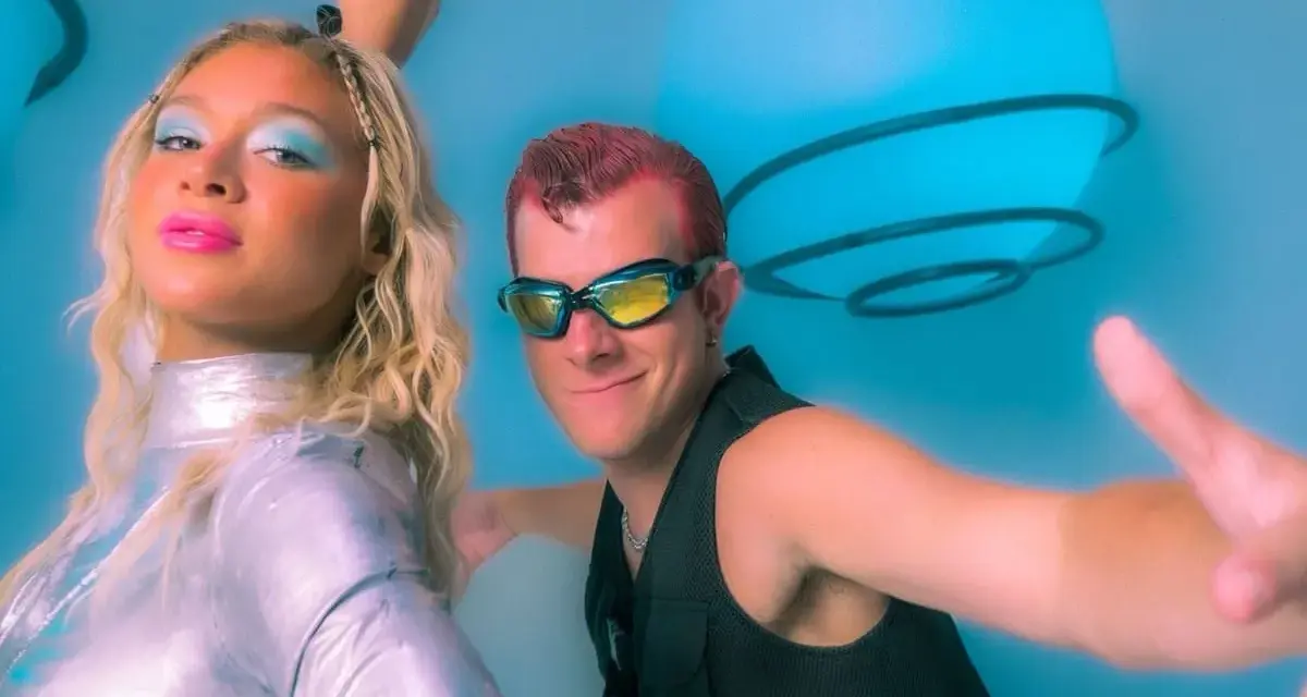 Un groupe hollandais des années 90, avec une femme au maquillage bleu vif et un homme aux lunettes futuristes, pose devant des sphères lumineuses bleues.