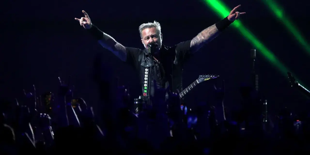 James Hetfield, un des membres de Metallica, salue la foule avec les cornes du diable, éclairé par des faisceaux verts.