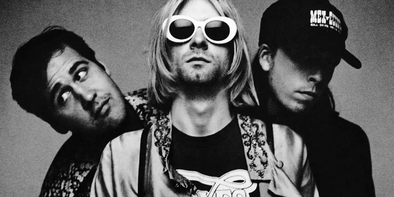 Les membres de Nirvana posent ensemble, Kurt Cobain au centre avec ses lunettes blanches iconiques.