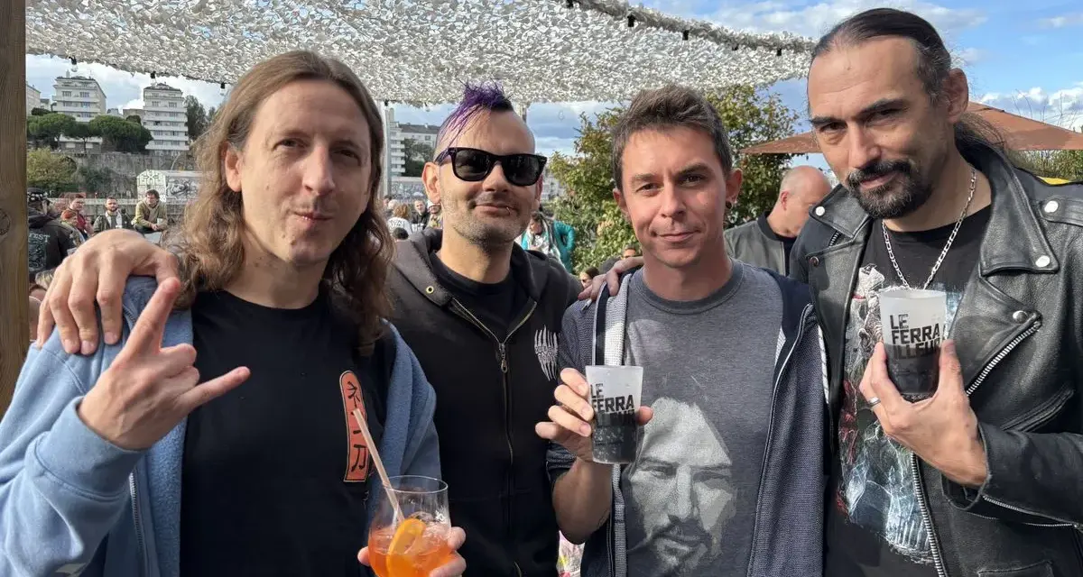 Quatre hommes, un groupe hollandais des années 80, posent avec des boissons. L'un fait un signe de rock.