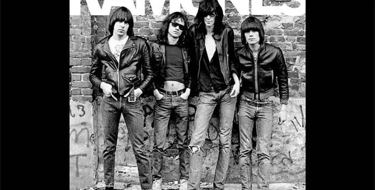 Les Ramones, quatre icônes punk en blousons de cuir et jeans, posent devant un mur de briques tagué.