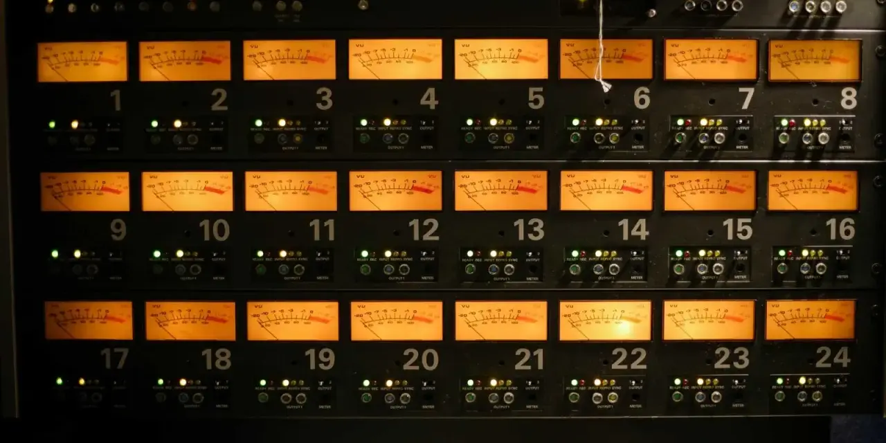 Rack d'équipements audio avec 24 vu-mètres orange illuminés, indiquant des niveaux sonores pouvant atteindre 76 décibels équivalents.