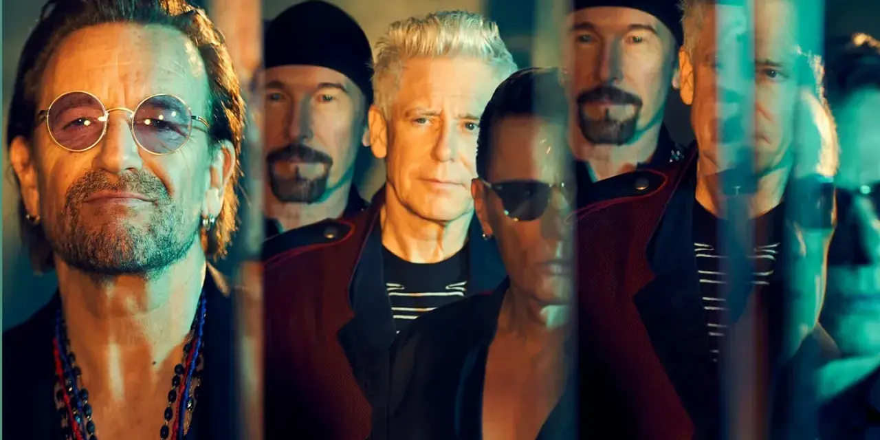 Le groupe U2, avec Bono au premier plan, pose en groupe, leurs visages reflétant une lumière tamisée.
