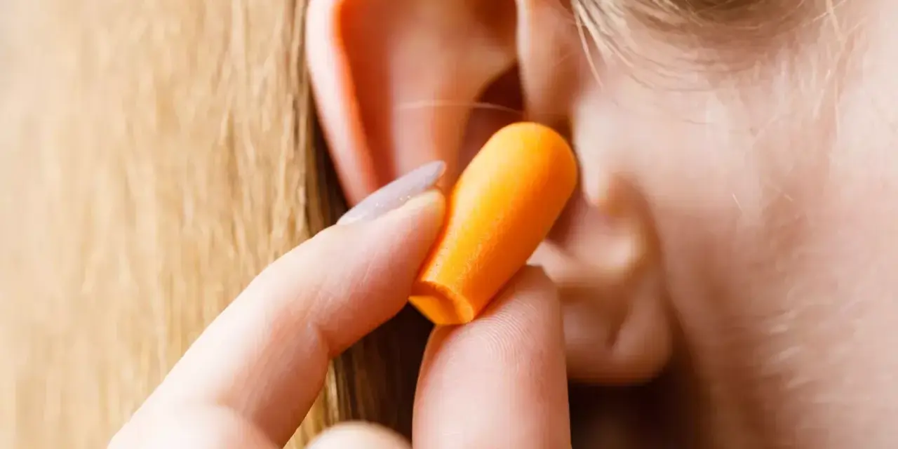 Une main insère une boule quies orange dans une oreille pour réduire les décibels.