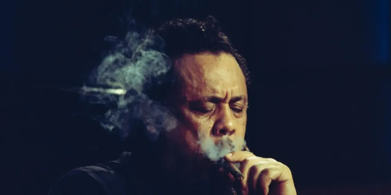 Charlie Mingus, le légendaire contrebassiste, exhale une fumée épaisse, les yeux clos, absorbé par sa musique.