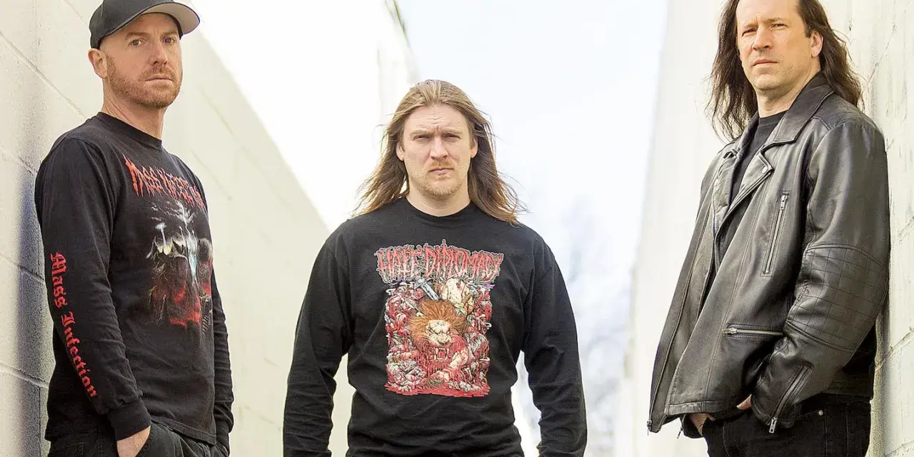 Trois hommes posent devant un mur. L'un porte un t-shirt avec une image de fœtus mourant.