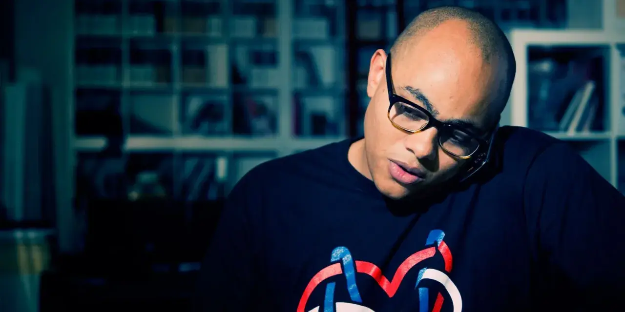Un homme chauve avec des lunettes, parlant au téléphone, porte un t-shirt avec un logo coloré. Il pourrait bien être celui qui a inventé le rap.