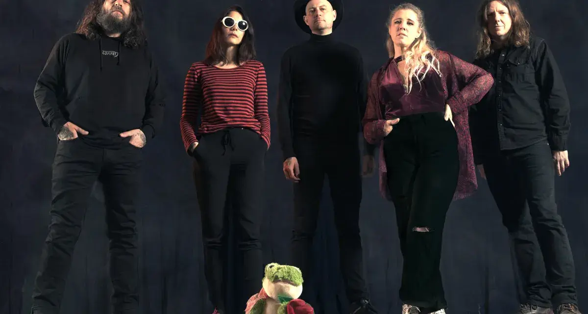 Cinq personnes se tiennent devant un fond sombre. Au premier plan, une grenouille en peluche tient une rose. Le groupe, comme un **crippled black phoenix**, semble prêt à s'envoler.