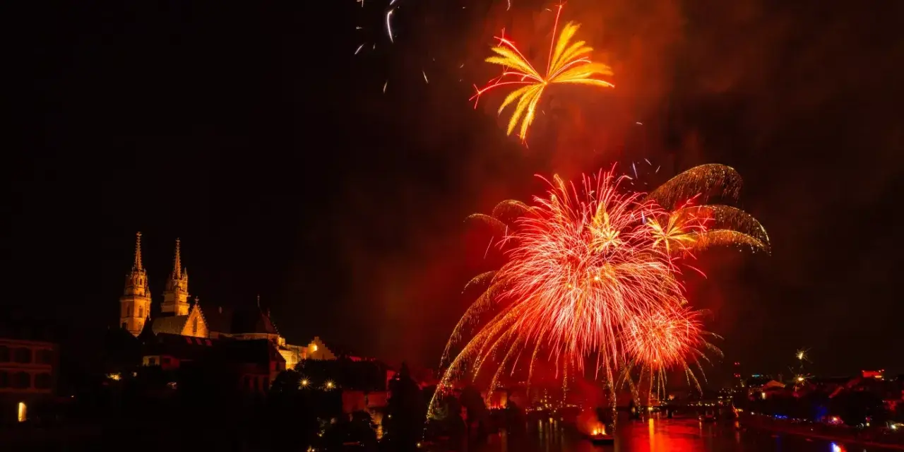 Feu d'artifice rougeoyant illuminant le ciel nocturne au-dessus d'une ville et d'une rivière. Le **décibel feu d'artifice** résonne dans l'air.