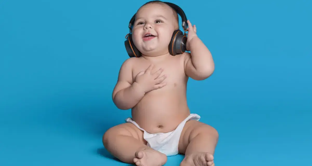 Un bébé souriant, en couche, écoute de la musique avec des écouteurs, le décibel maximum pour un bébé est à éviter.