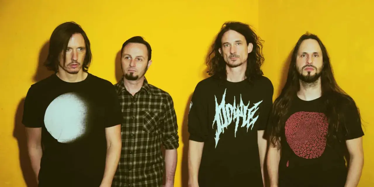 Quatre hommes aux cheveux longs posent devant un fond jaune vif. Leurs t-shirts portent des graphismes distinctifs, évoquant l'énergie brute du magma et la puissance de Gojira.