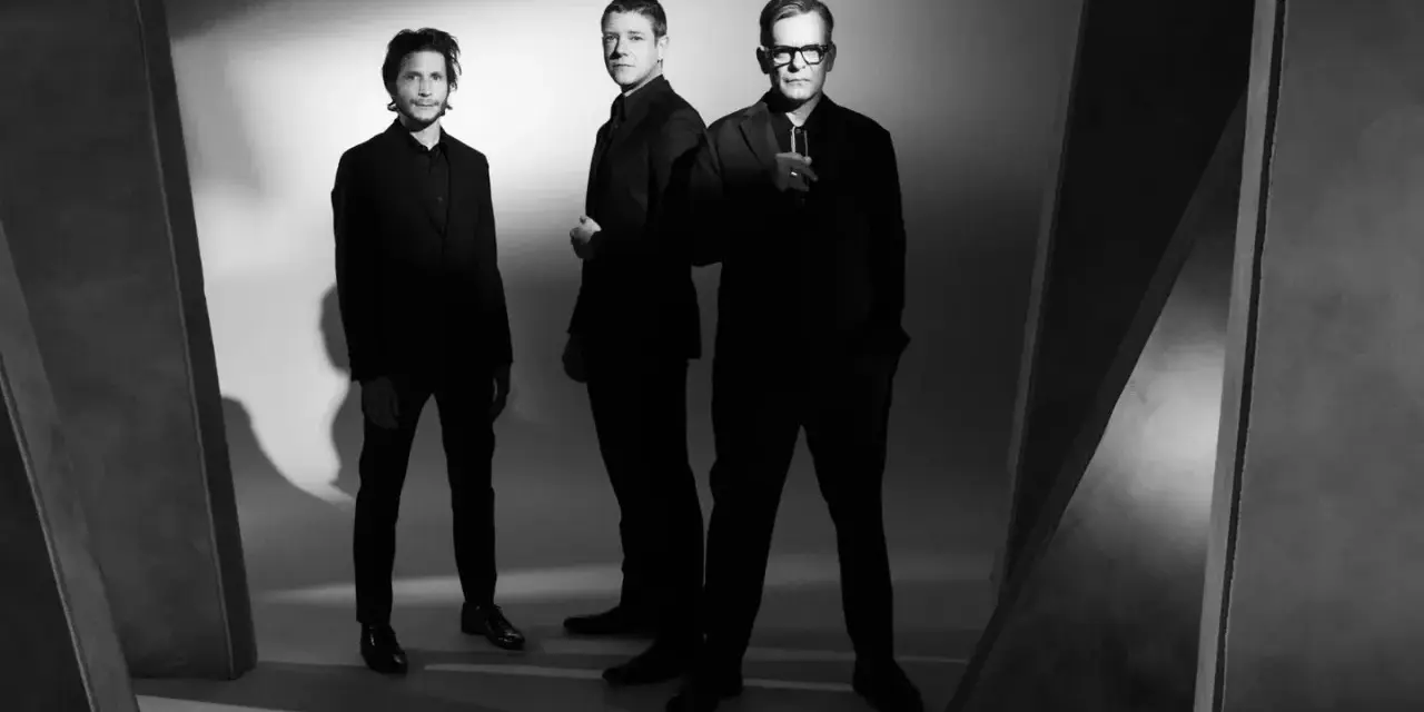 Le groupe Interpol pose en noir et blanc, trois hommes en costumes sombres, dans une ambiance épurée et artistique.