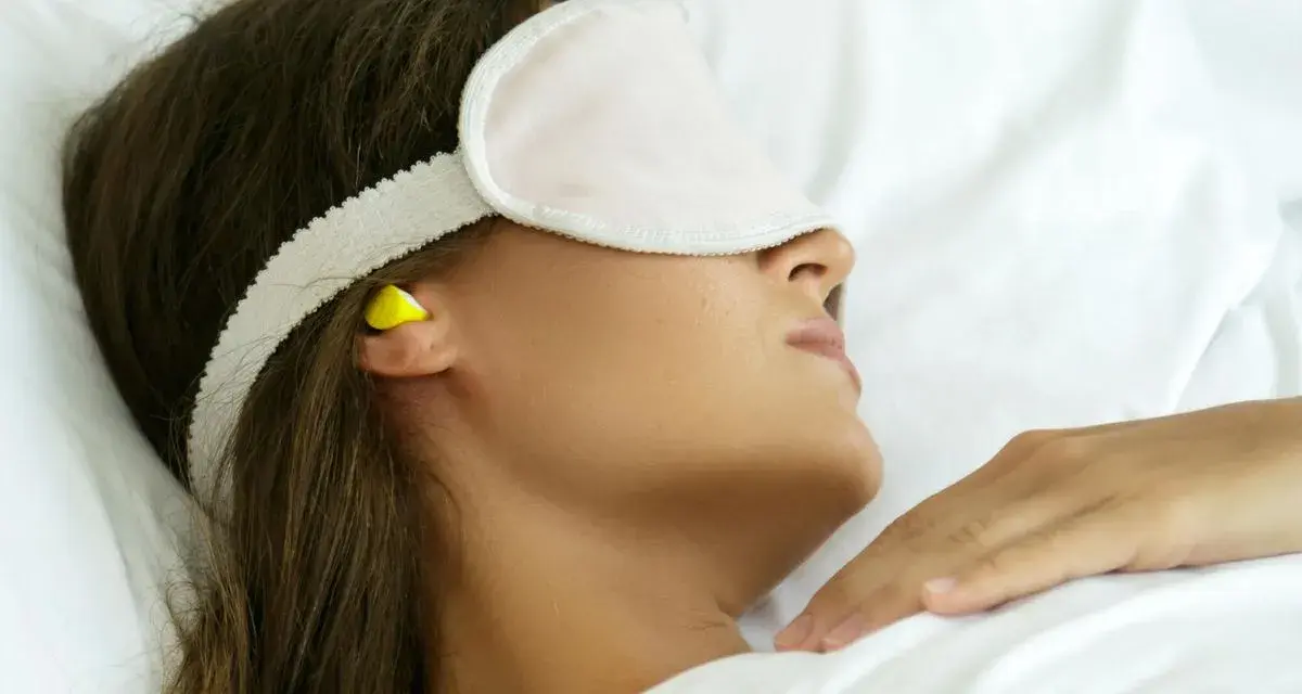 Femme dormant avec un masque et des boules quies pour éviter le bruit, utile en cas d'otite ou pour un sommeil paisible.