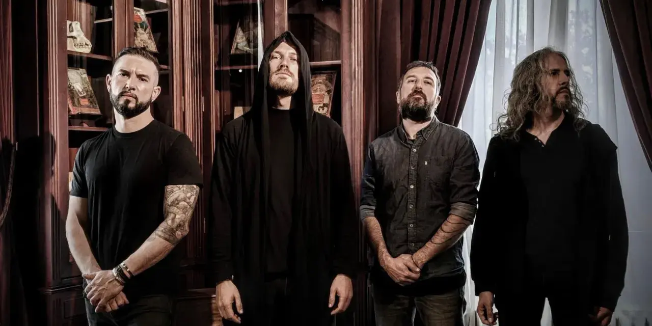 Quatre musiciens, dont un avec une capuche, posent devant des étagères remplies de livres. Ce groupe metal français connu dégage une aura mystérieuse.