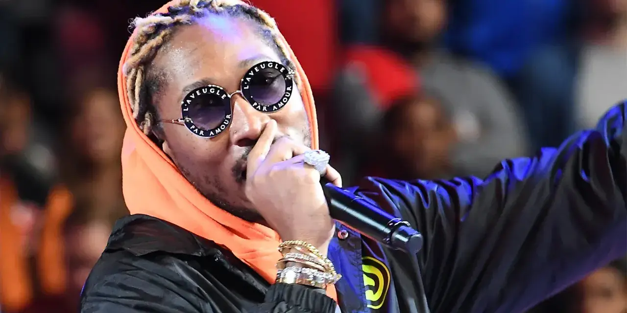 Un rappeur à la mode, avec des lunettes stylées et de nombreux bijoux, chante sur scène.