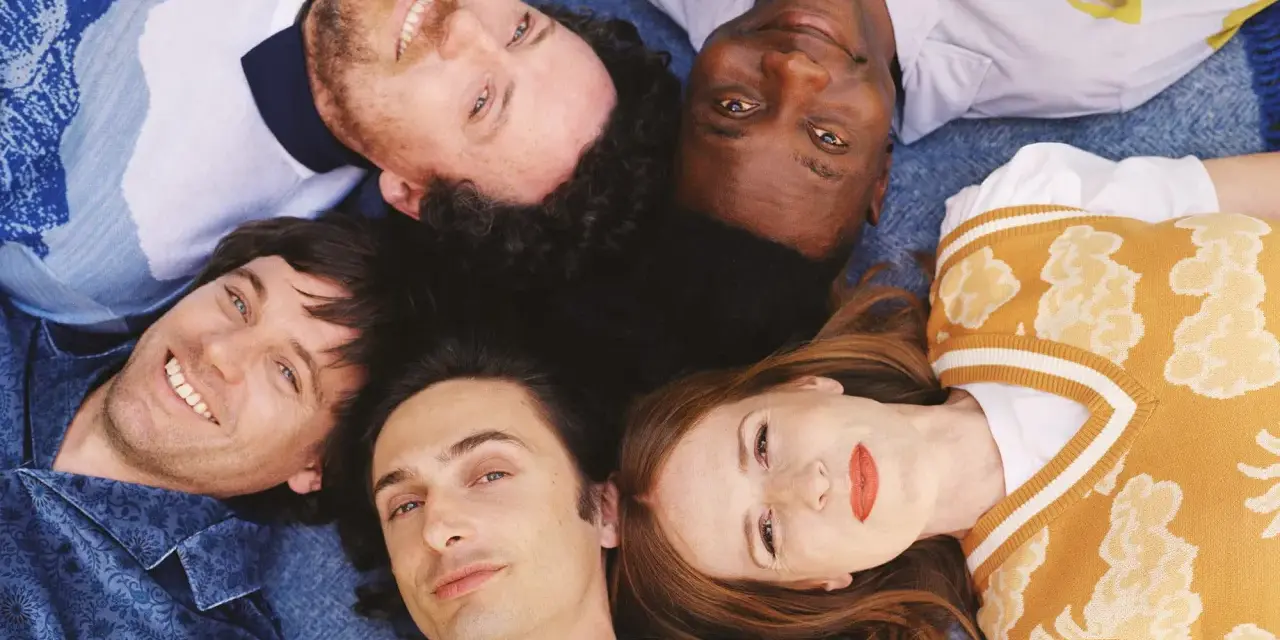 Les membres de Metronomy, cinq visages souriants, forment une étoile sur un fond bleu.