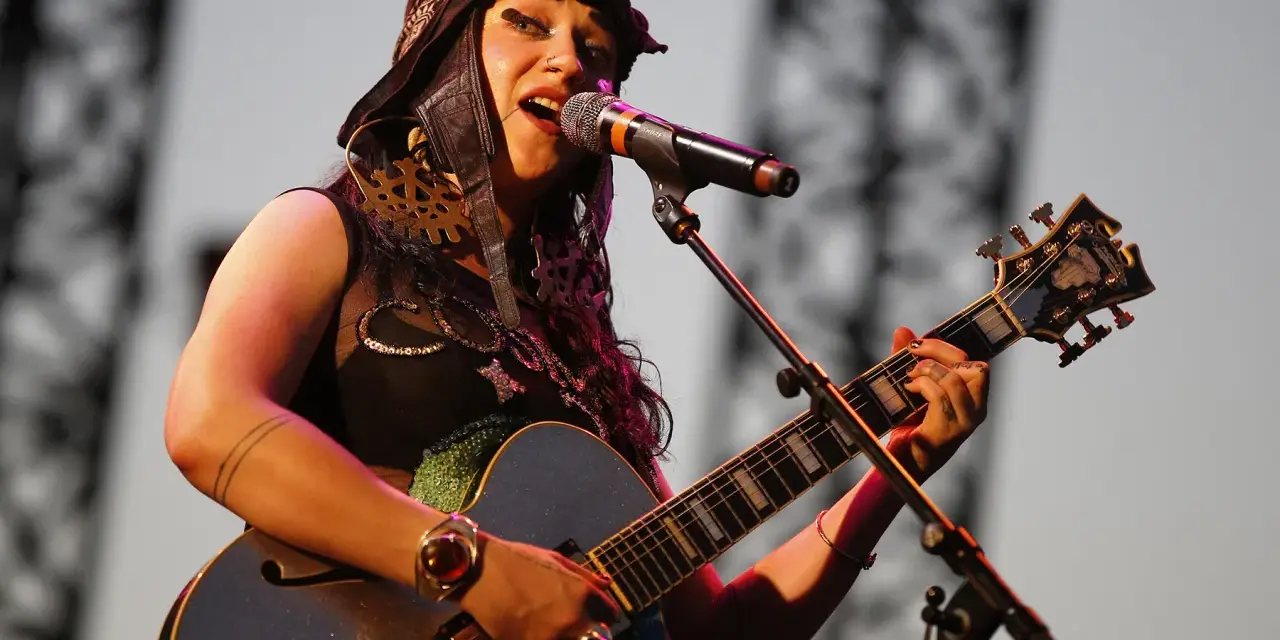 Une artiste de Hiatus Kaiyote, casquette sur la tête, chante et joue de sa guitare bleue étincelante sur scène.
