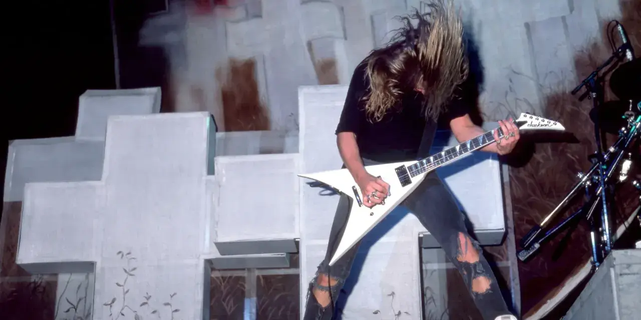 Guitariste aux cheveux longs, en plein solo, tel un maître des marionnettes sur scène.