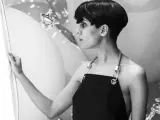 Fatima Al Qadiri, artiste à la coupe courte, porte un tablier noir, regardant une œuvre abstraite.