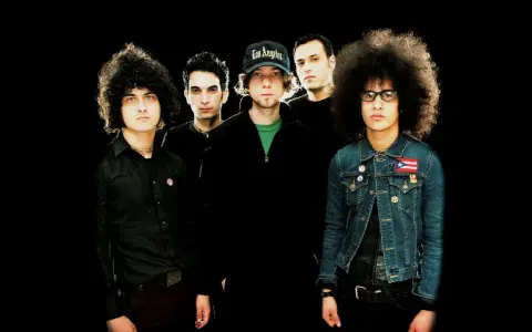 Cinq musiciens, dont certains avec des coiffures afro, posent pour une photo de groupe. L'un porte une casquette "Los Angeles". Ils sont prêts pour une soirée **at the drive in**.