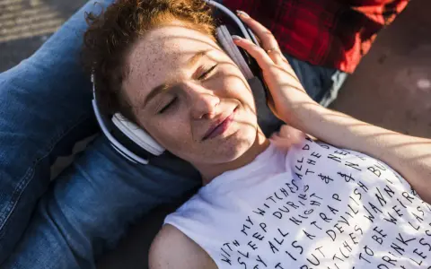 Jeune femme aux taches de rousseur, écouteurs blancs, profitant de la musique. Le volume est à 95 db équivalent, elle semble détendue.