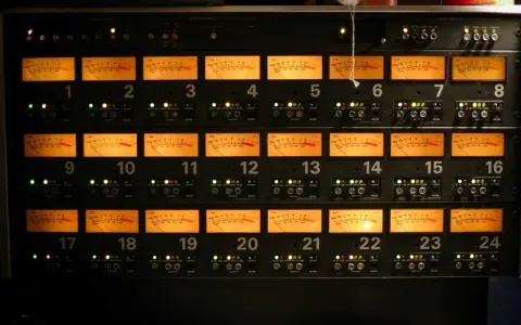 Panneau d'équipement audio avec 24 indicateurs VU orange, chacun affichant un niveau sonore, certains proches de 0 dB, équivalent à 64 décibels.