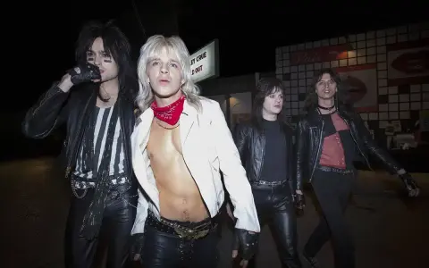 Quatre membres du groupe Motley Crue, vêtus de cuir noir et de maquillage, marchent dans la nuit.