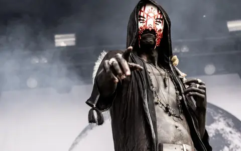 Un membre d'un groupe metal masqué, le visage peint de rouge et blanc, pointe du doigt.