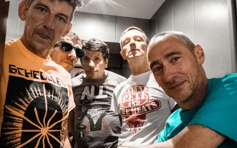 Cinq hommes aux têtes brûlantes, certains souriants, d'autres plus intenses, posent pour un selfie. Leurs t-shirts affichent des graphismes variés.