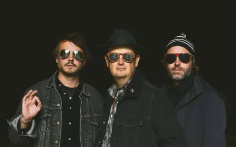 Trois hommes, lunettes de soleil, chapeau, bonnet. Ils ont l'air cool, pas comme des zombies.