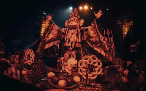 Un personnage masqué, drapé dans des tissus ornés, semble présider un rituel. Autour de lui, des offrandes de fruits, des serpents stylisés et des symboles sacrés évoquent un culte du feu mystérieux.