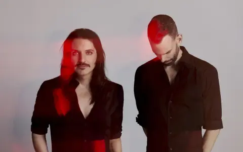 Les membres de Placebo, Brian Molko et Stefan Olsdal, posent en noir et blanc avec des éclats de lumière rouge.