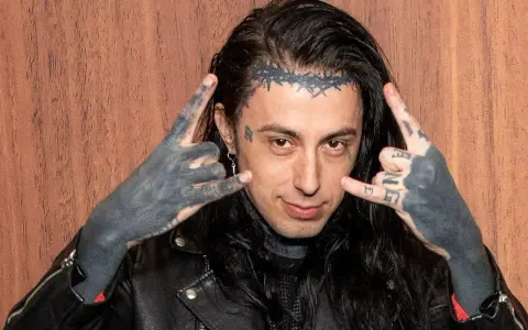 Un membre de Falling In Reverse, avec des tatouages sur le visage et les mains, fait le signe des cornes.
