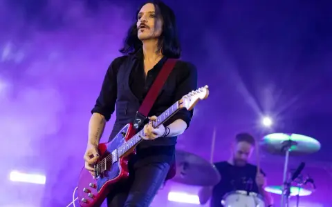 Brian Molko, le chanteur de Placebo, joue de la guitare rouge sur scène, éclairé par des lumières violettes.