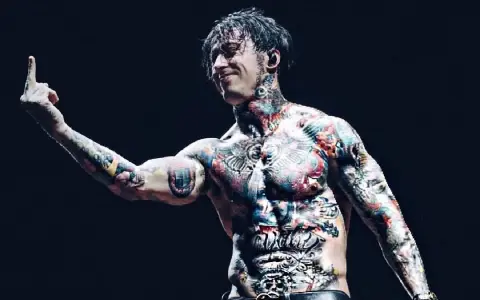 Le chanteur de Falling In Reverse, Ronnie Radke, torse nu et couvert de tatouages colorés, lève le majeur sur scène.