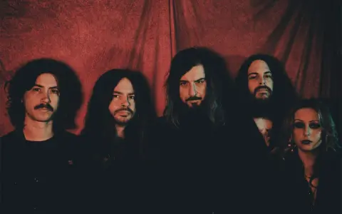 Cinq membres du groupe Uncle Acid and the Deadbeats posent devant un rideau rouge.