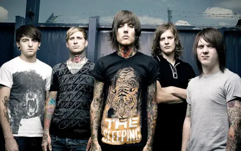 Cinq membres du groupe Bring Me The Horizon posent devant une clôture. Le chanteur porte un t-shirt avec un tigre et le texte "The Sleeping".