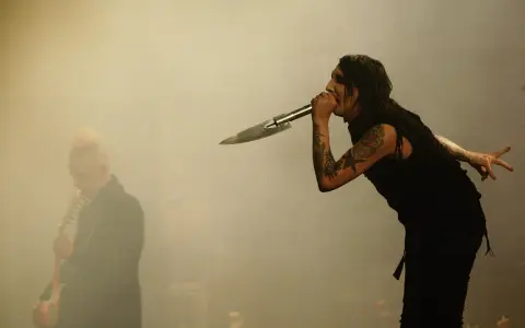 Marilyn Manson chante dans un micro en forme de couteau, un autre musicien est flou à gauche. L'ambiance d'un concert de Marilyn Manson album.