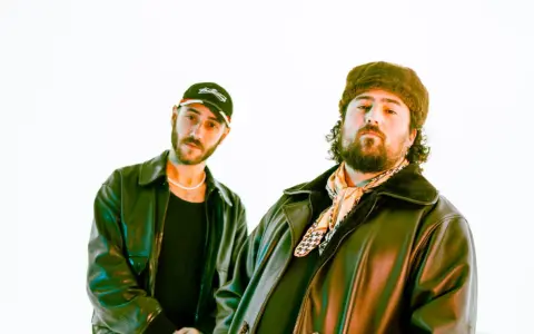 Deux DJ les plus connus, l'un porte une casquette et l'autre un bonnet en fourrure, posent devant un fond blanc.