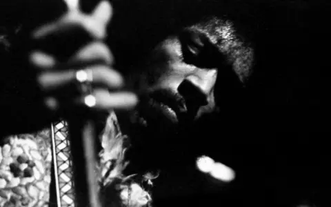 Gros plan en noir et blanc de Jimi Hendrix jouant de la guitare, évoquant l'esprit de ses albums légendaires.