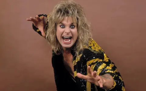 Ozzy Osbourne, le prince des ténèbres, avec sa chevelure blonde ébouriffée et un regard intense, porte une veste noire ornée de motifs dorés.