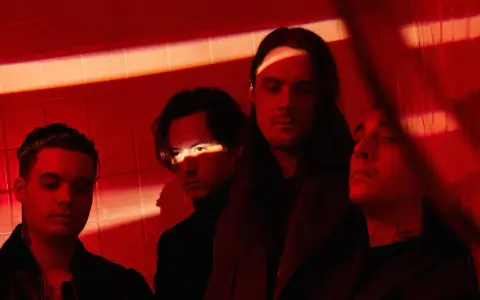 Les membres de Bad Omens posent dans une ambiance rouge intense, éclairés par des ombres dramatiques.