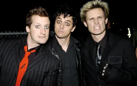 Les membres de Green Day, Billie Joe Armstrong, Mike Dirnt et Tré Cool, posent ensemble. Armstrong a les yeux écarquillés, Dirnt a un regard intense et Cool fait une grimace.